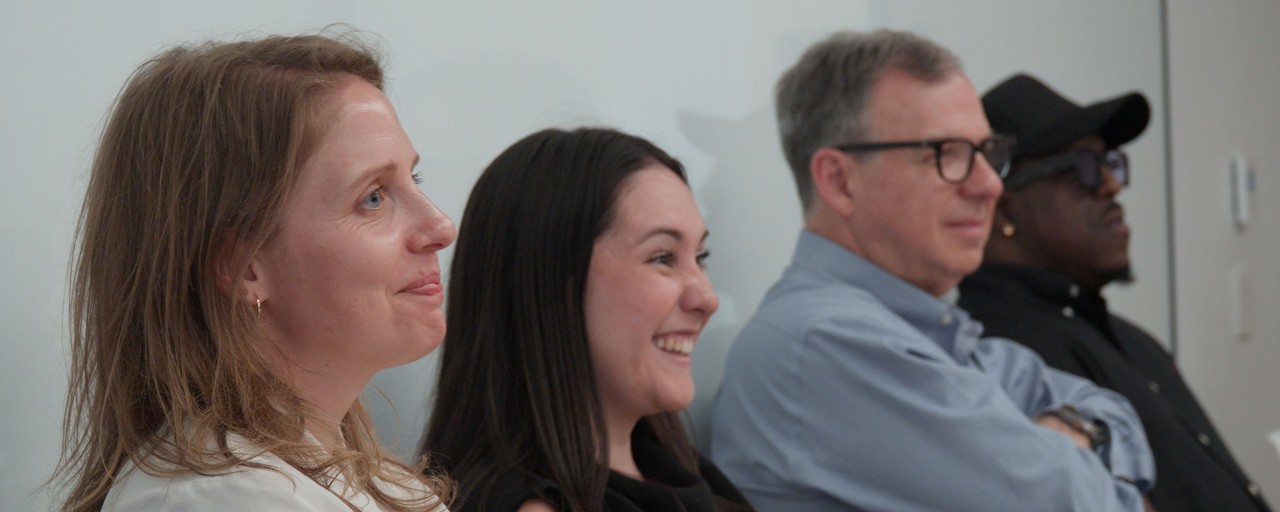 Two people examining sticky notes on a glass wall in an office setting.