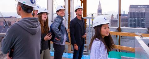nyu students with hardhats at a contruction site rooftop