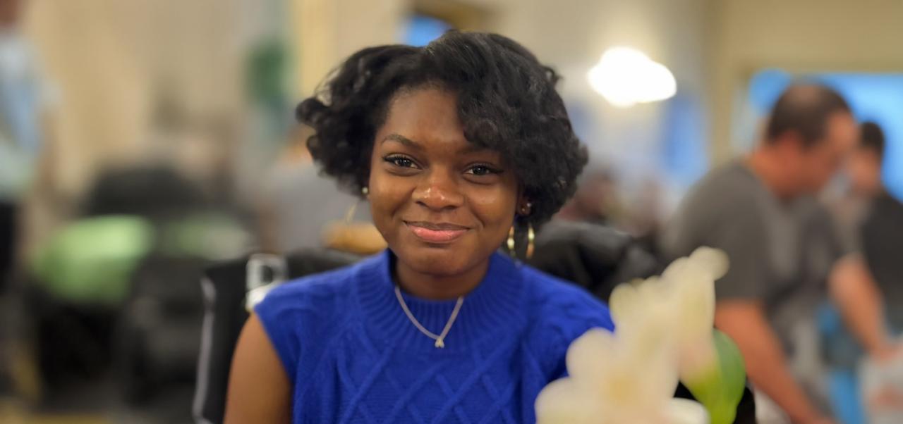 NYU SPS Jonathan M. Tisch Center of Hospitality alumnus Angelique Nicole Banks smiles for the camera while attending a formal event and blurred people buzz around in the background.