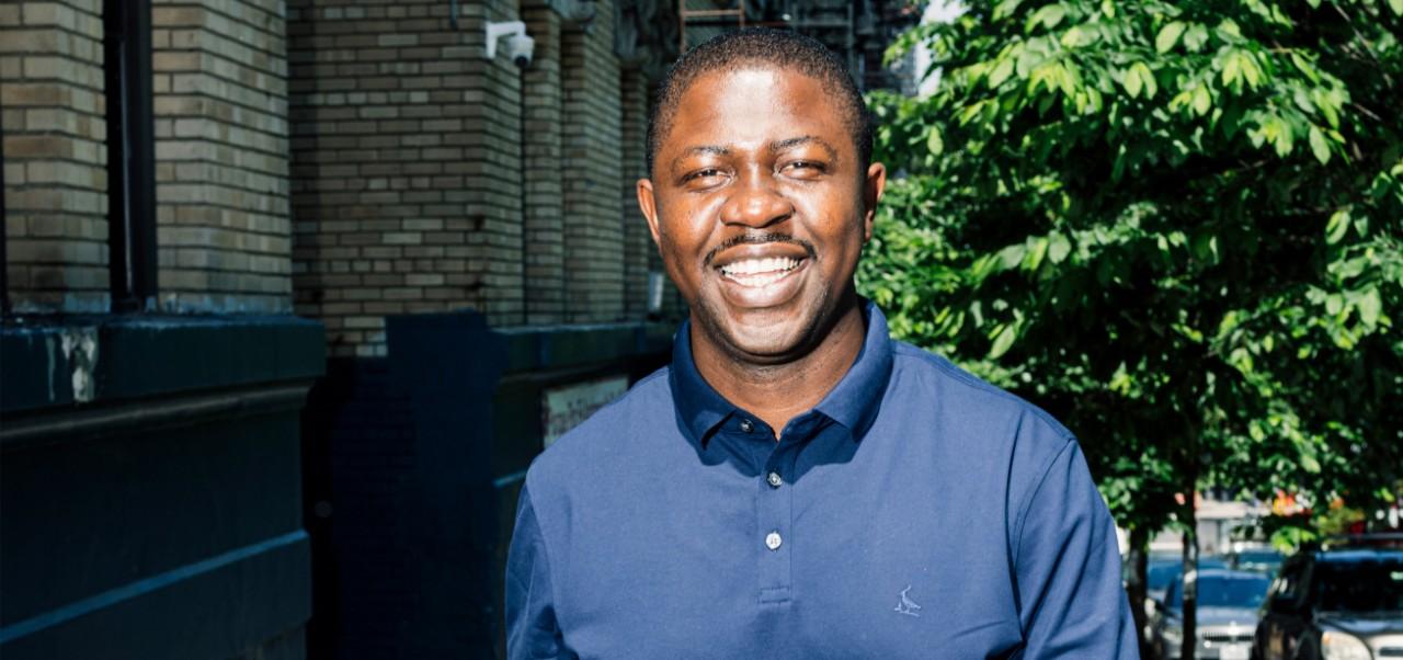 Edafe Okporo, NYU SPS Division of Programs in Business alumnus, smiles for the camera on a tree-lined New York City street.