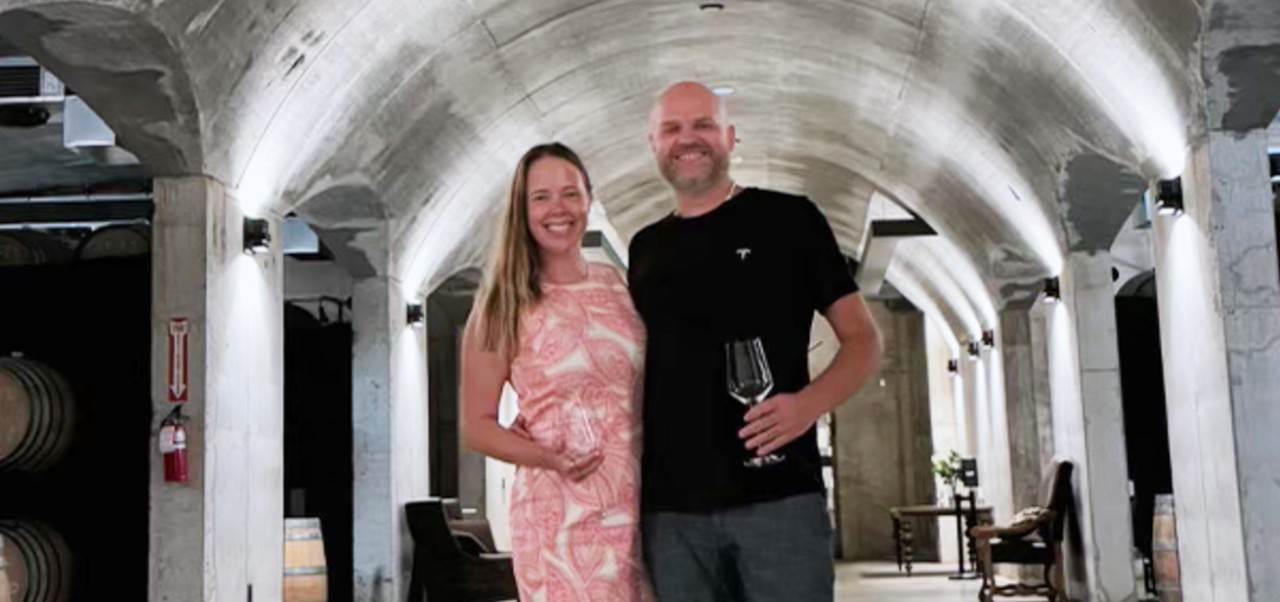 Lindsay Saunders, student at the Division of Programs in Business, NYU SPS, smiles for the camera with her partner while both holding wine glasses in a winery cavern.