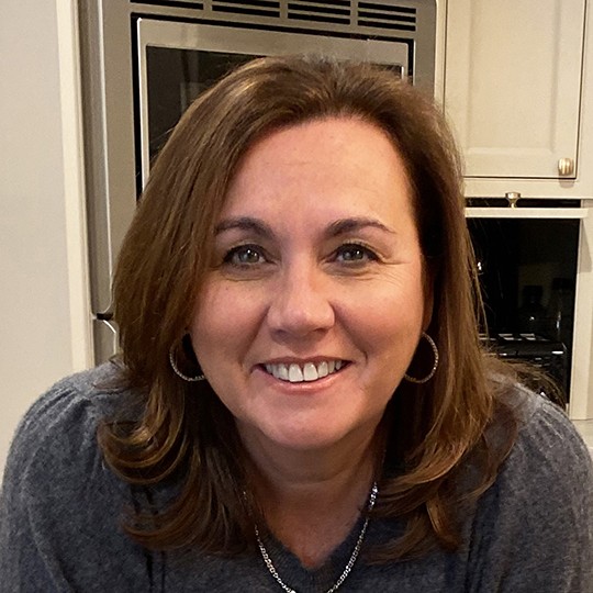 NYU SPS Division of Programs in Business alumnus Noreen Beaman poses for a photo while holding a bouquet of flowers in her kitchen.