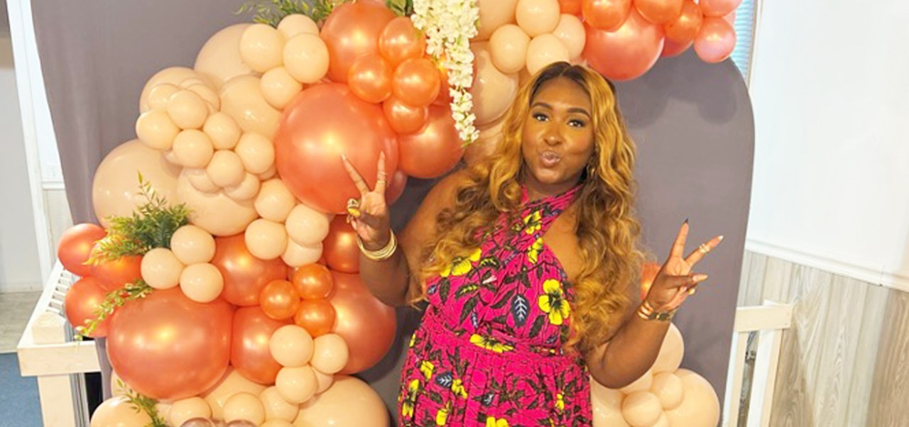 BA in Social Sciences alum Shakia Rose poses with peace signs in front of a balloon arch