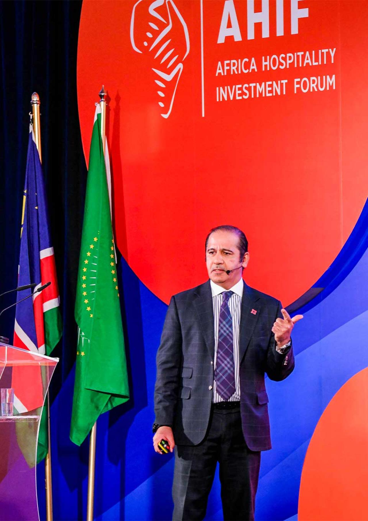 Turab Saleem at the Africa Hospitality Investment Forum with a logo backdrop and flags.