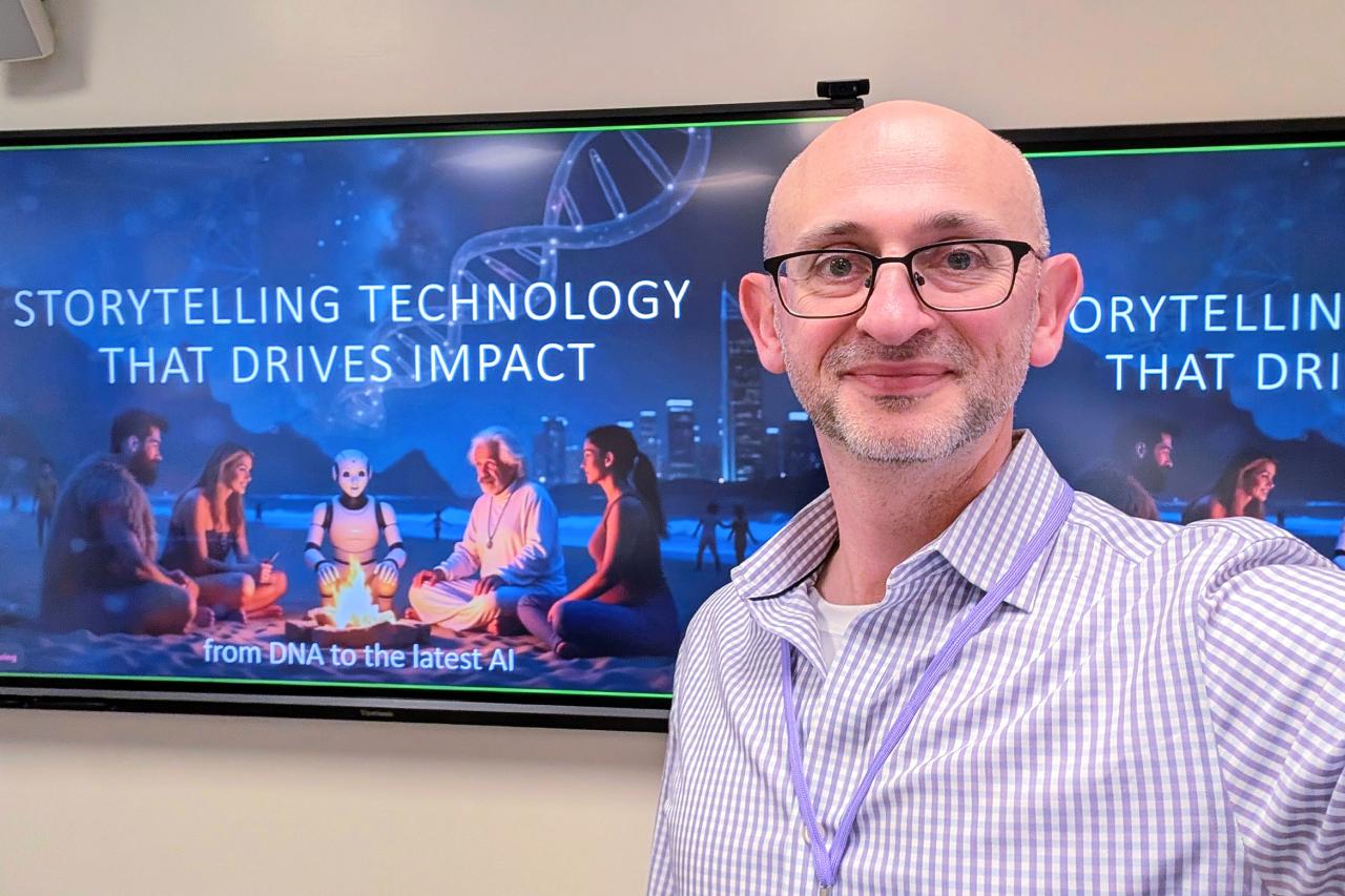 NYU SPS Continuing Education instructor Boris Keivsky snaps a selfie in front of a poster that reads Storytelling Technology that Drives Impact