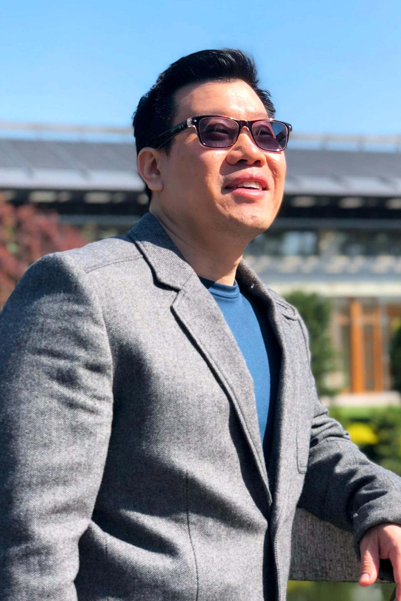 Jimmy Pang, continuing education faculty member at NYU SPS smiles upward toward the sun while wearing sunglasses