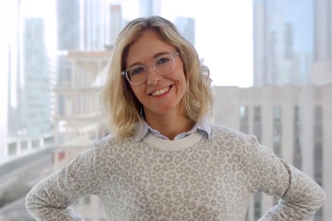 NYU SPS faculty member Kathleen Murphy smiles for a headshot in front of a window overlooking an NYC cityscape