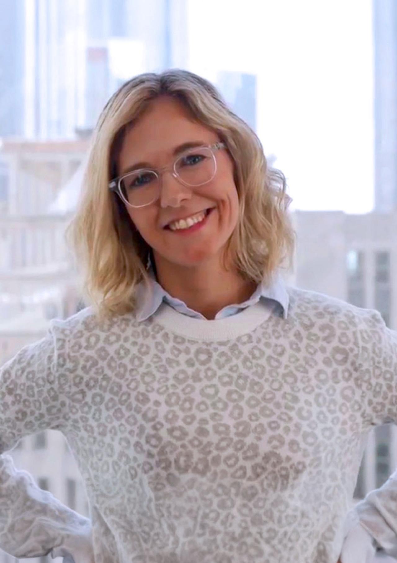 NYU SPS faculty member Kathleen Murphy smiles for a headshot in front of a window overlooking an NYC cityscape