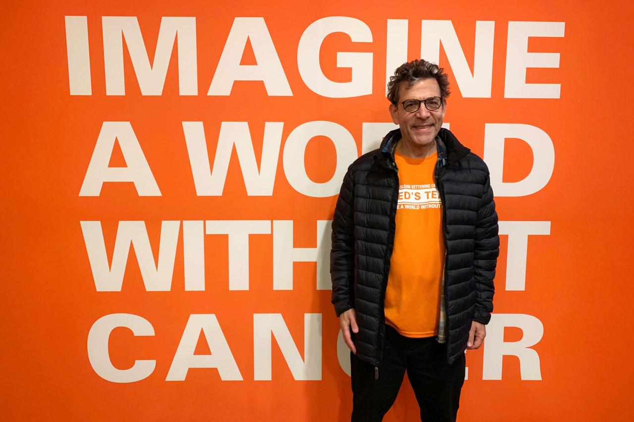 NYU SPS CE instructor Robert Marino smiles for a photo in front of an orange wall that reads "imagine a world without cancer"