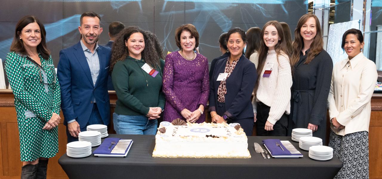 Andrea L Chambers, Clinical Assistant Professor, Center for Publishing and Applied Liberal Arts, NYU SPS, smiles for the camera while standing around a large sheet cake with colleagues.