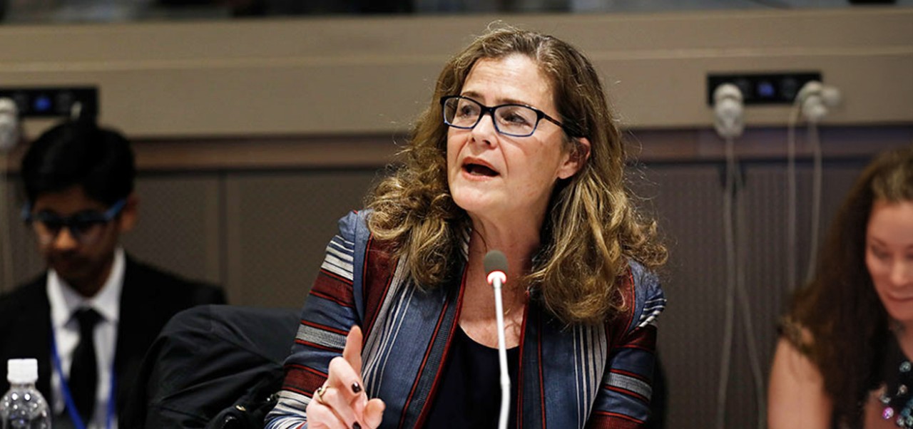 Anne Marie Goetz speaks into a microphone at the UN Women Action in Policy event with two people blurred in the background