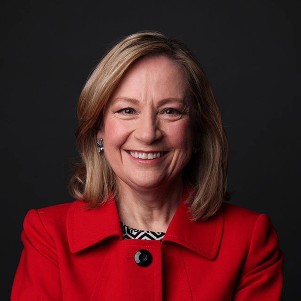 Headshot of Beverly Tarulli who wears a red jacket in front of a black background