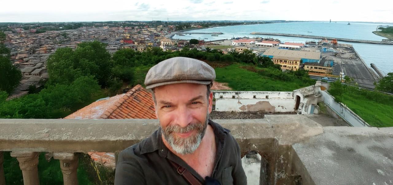 Christopher T Gaffney, Clinical Professor, Jonathan M. Tisch Center of Hospitality at NYU SPS, smiles for the camera on a balcony overlooking a residential bay.