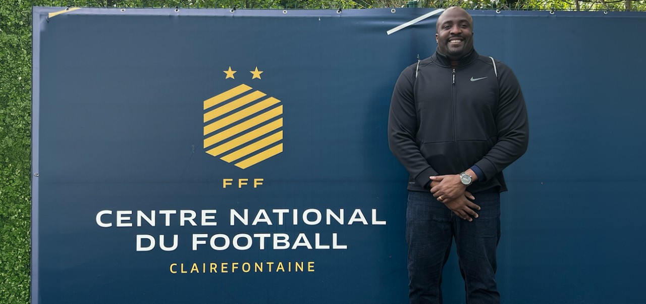 Daniel G Kelly II, Clinical Professor, Preston Robert Tisch Institute for Global Sport, NYU SPS, poses for a photo in front of a advertisement for the Centre National du Football, Clairefontaine.