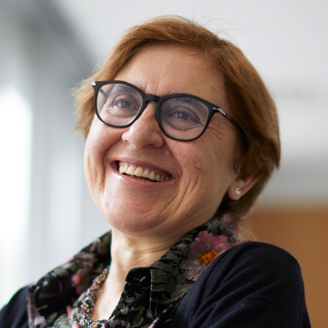 While sitting in a burgundy leather chair, Donatella Delfino smiles into the distance while posing for a headshot