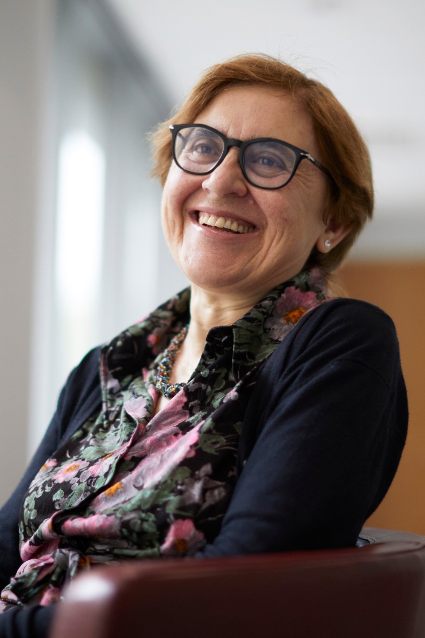 While sitting in a burgundy leather chair, Donatella Delfino smiles into the distance while posing for a headshot