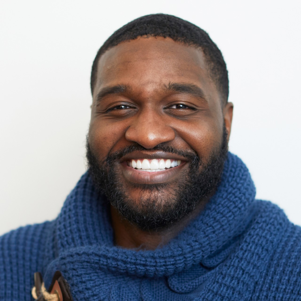 Eli Joseph smiles for a headshot while wearing a blue sweater in front of a white background