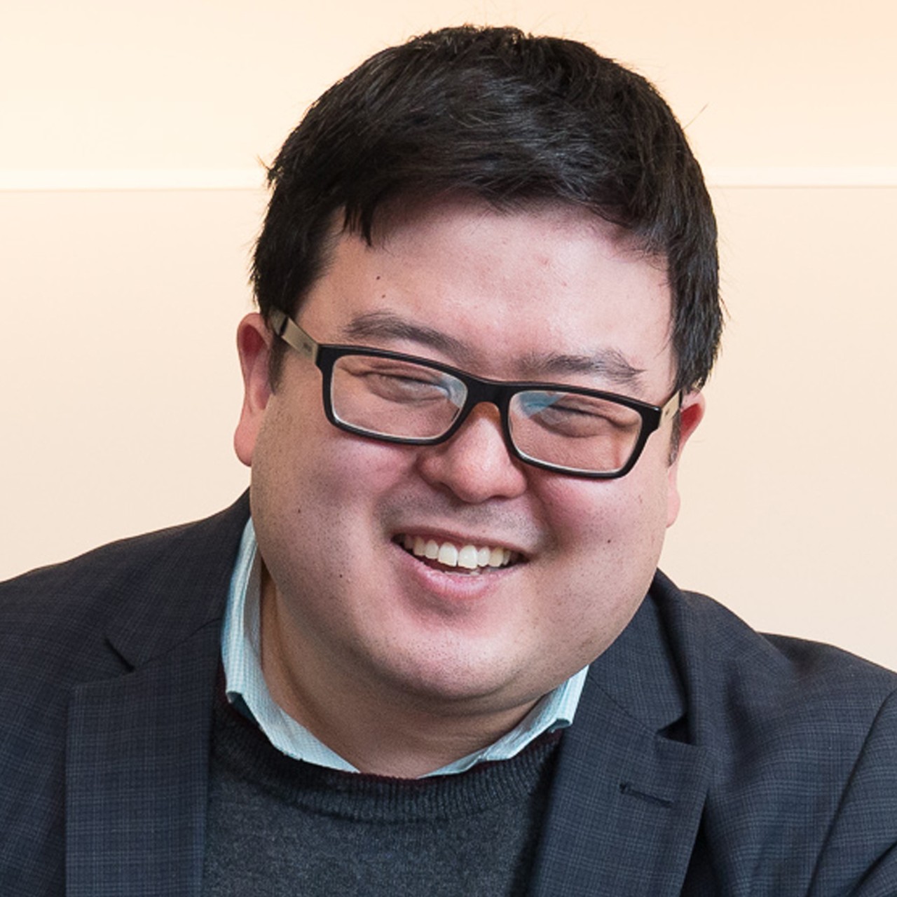 Jason Chung smiles while wearing a dark grey blazer and grey sweater for a headshot in front of a solid white background