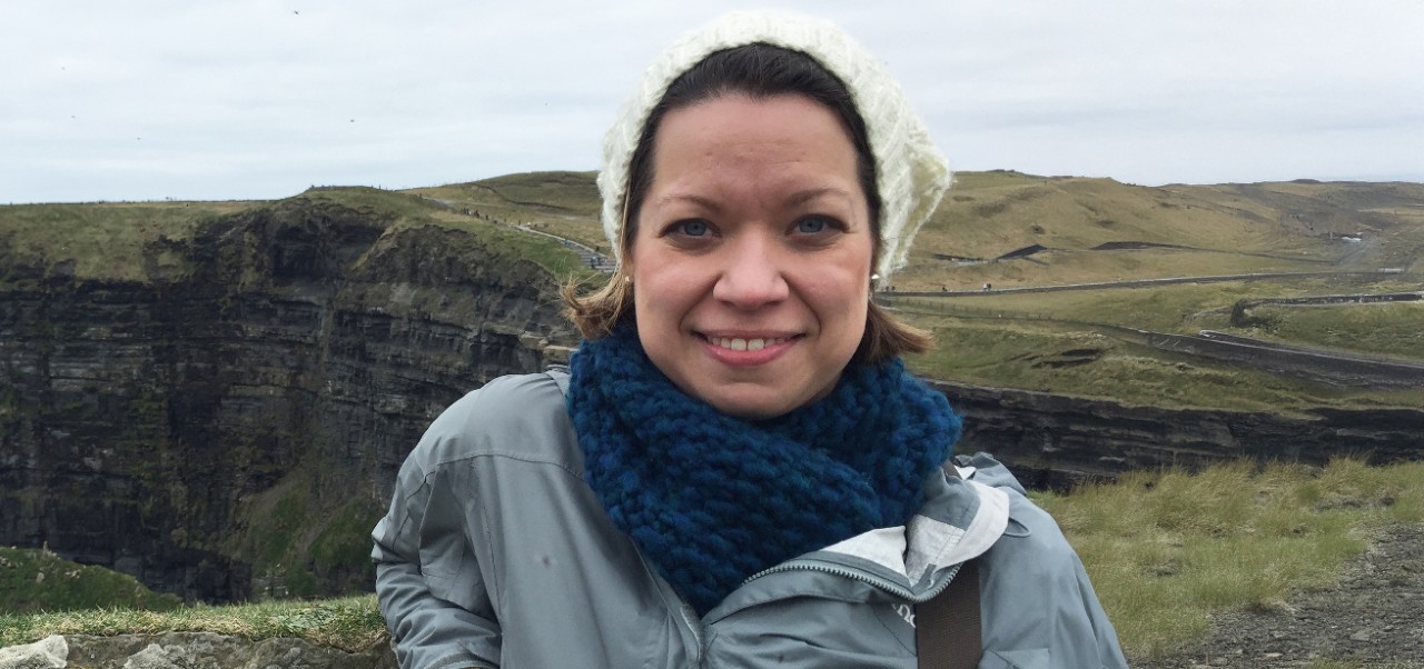 Lara Romanowski, Adjunct Instructor, Center for Applied Liberal Arts, NYU SPS, takes a selfie in front of a rocky cliff in Iceland.