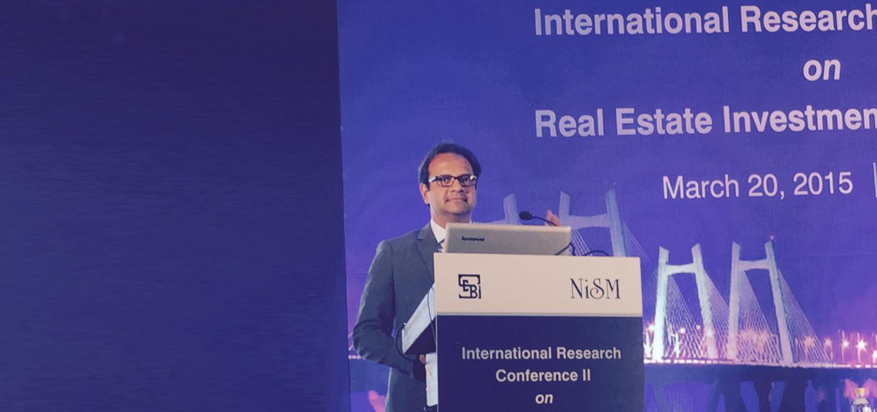 Manish Srivastava, Clinical Professor of Global Real Estate Finance, Investments, and Urban Development at the Schack Institute of Real Estate, NYU SPS, gives a presentation at a lectern during a 2025 conference on real estate.