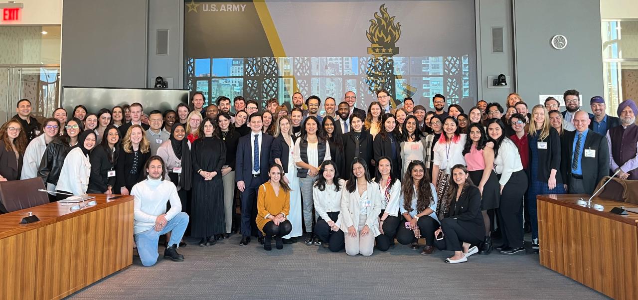 Mary Beth Altier smiles in a blue dress with a river and a bridge behind her.