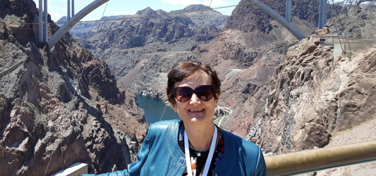 Roxana smiles in a blue jacket with mountains behind her while on an interpretation assignment at the Hoover Dam.