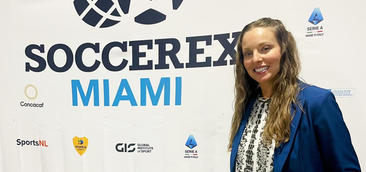 Sabrina Carrozza smiles next to a Soccerex Miami banner