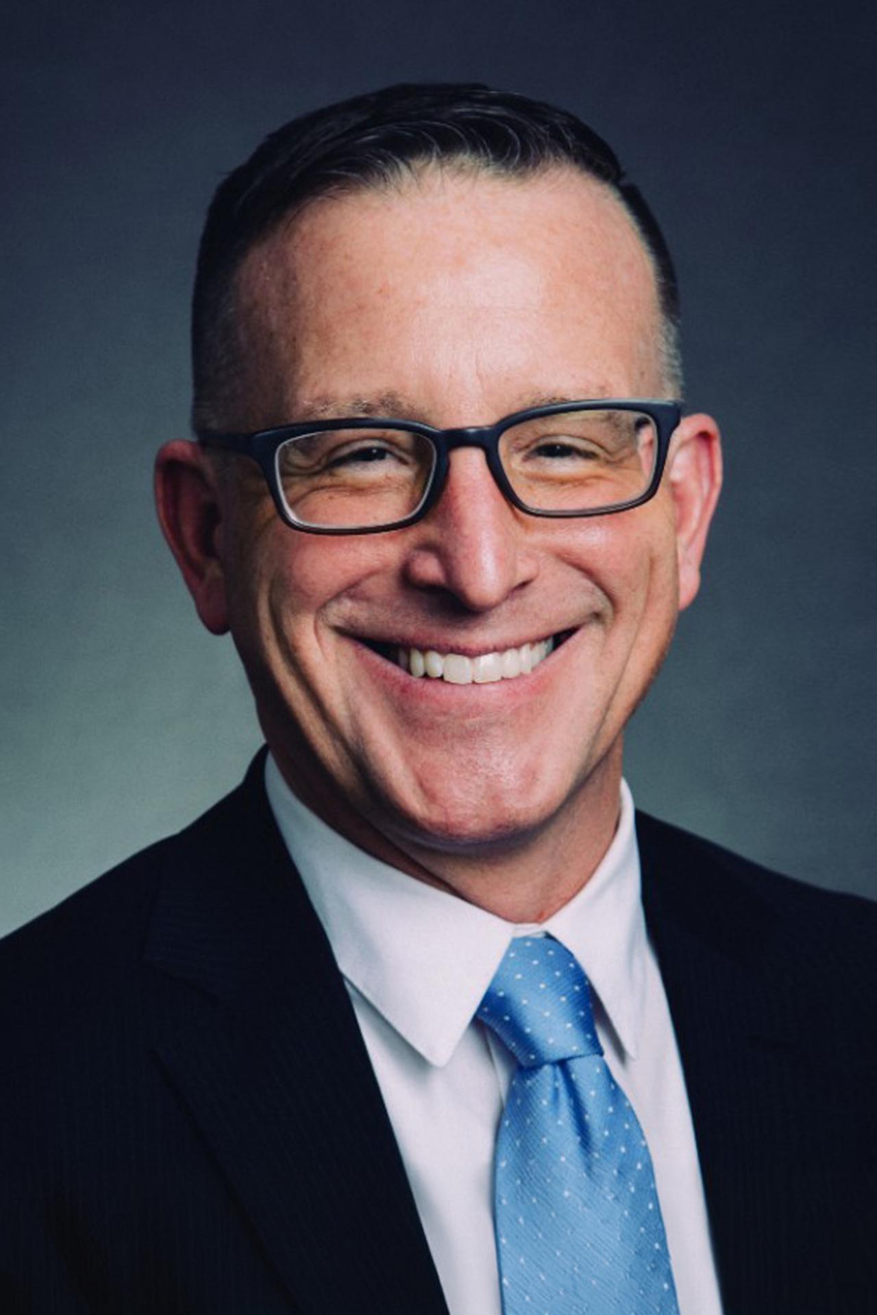 Headshot of Timothy Savage smiling in glasses and a suit
