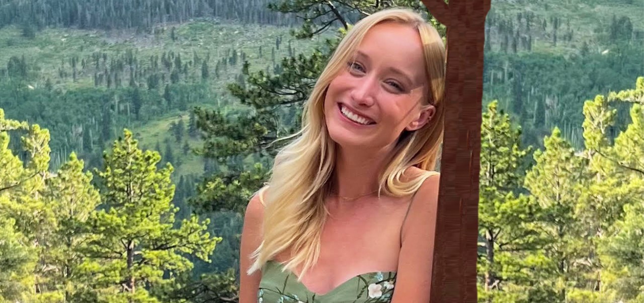Jane Griffin, student at the Center for Publishing and Liberal Arts at NYU SPS, smiles for the camera in front of an urban body of water, with a brick high rise in the background.