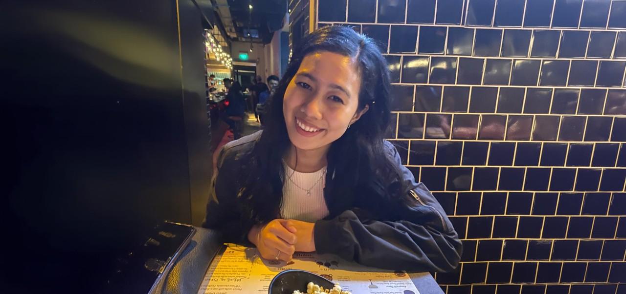 Nurul Syuhaidah Binte Senin, Jonathan M. Tisch Center of Hospitality at NYU SPS student, smiles for the camera at a restaurant while perusing a menu.