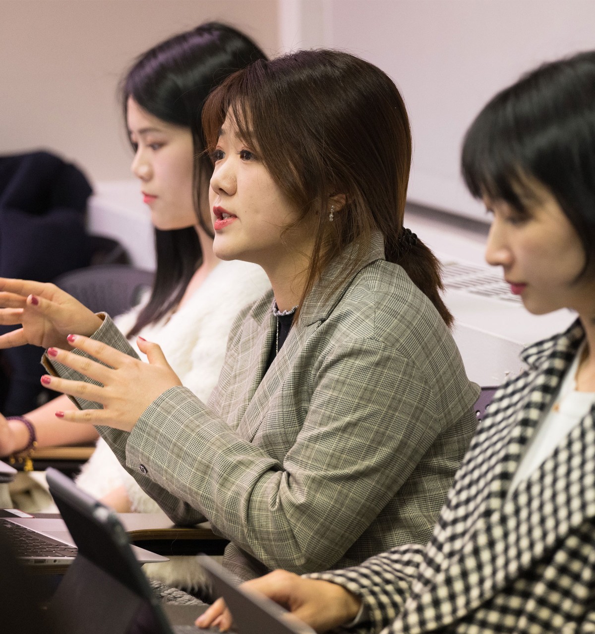 Woman in middle speaking with hand gestures, two women on her sides are looking down at their laptops