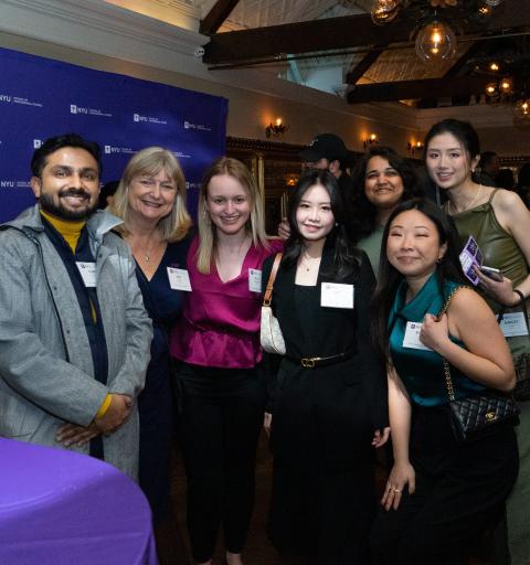A group of people smiling at a networking event, standing together in front of a purple NYU Stern banner.