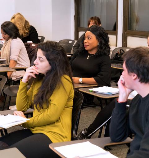 Several NYU SPS Center for Global Affairs scholarship students sit behind desks in a classroom while listening to a lecture, some taking notes