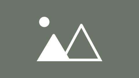 A flamboyant, historic building sitting on a California beach behind its own reflection on the ocean.