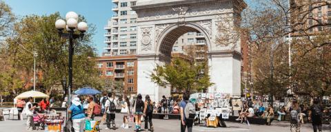 People enjoying a sunny day at Washington Square Park near NYU, with street vendors and the iconic arch in the background.