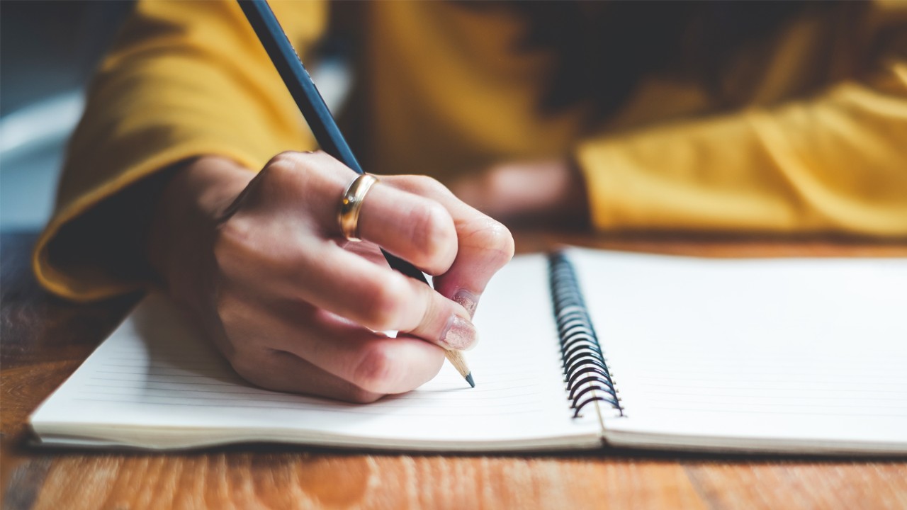 A right-handed student writes with a pencil in a notebook.