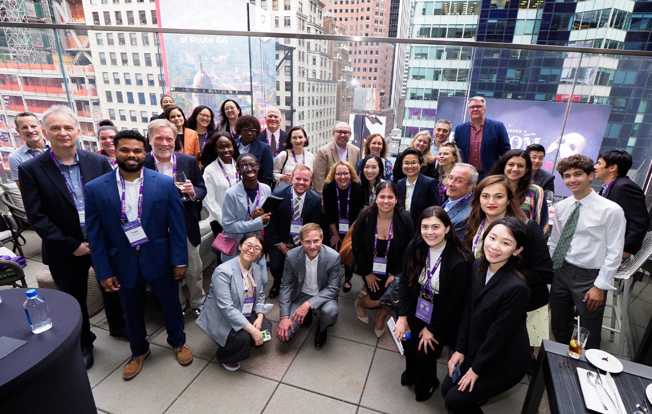 A large group of AAS in Hospitality students pose for a photo on a rooftop with a cityscape behind them