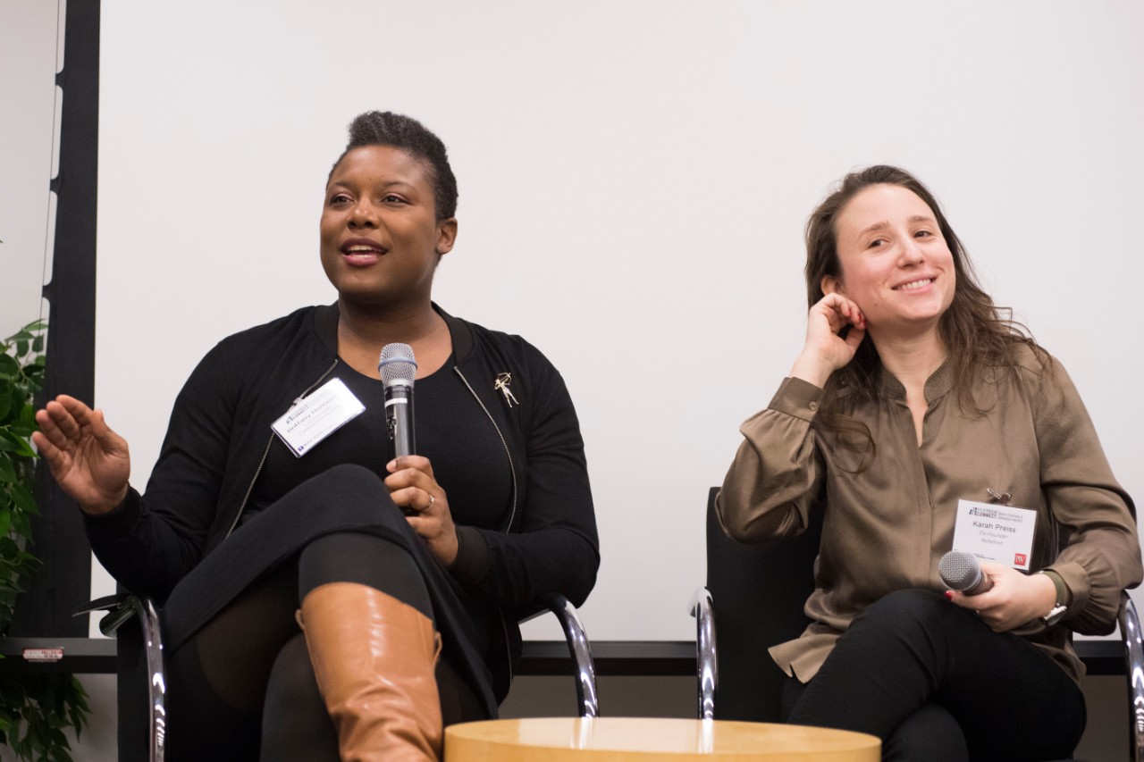 2 women sitting, both with microphones in their hands