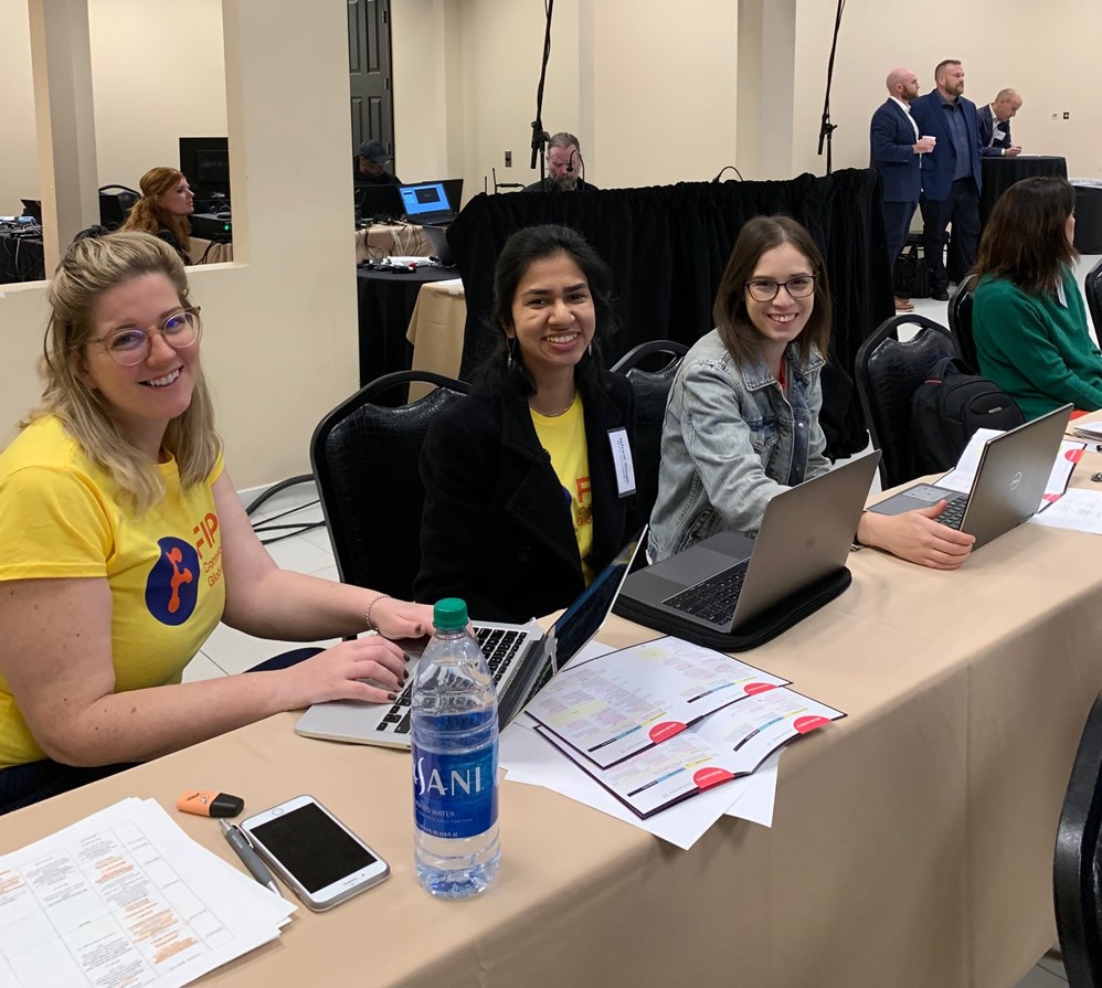 Emily Joshu, Ishani Singh, and Emily Smibert serving as conference volunteers at their workstations