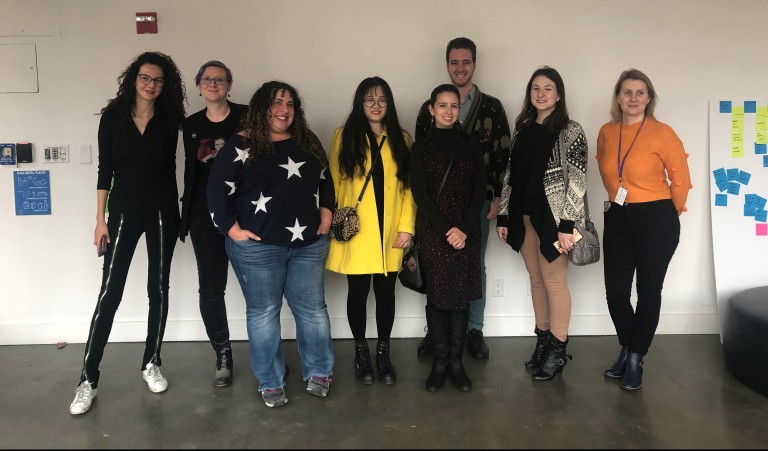 8 students standing and posing in front of a white wall