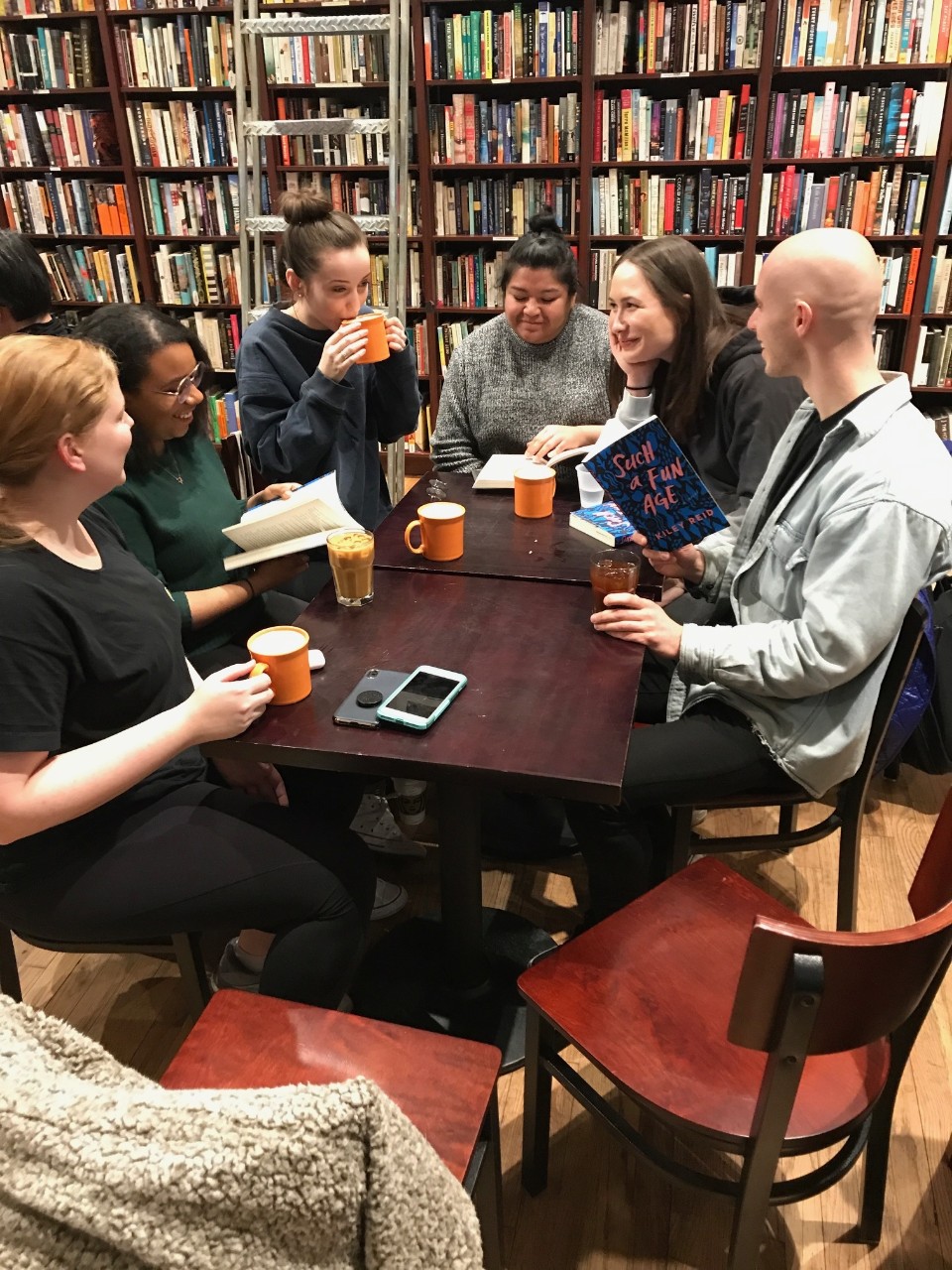 PSA members sit around a table while talking and holding books and beverages in a room filled with bookcases