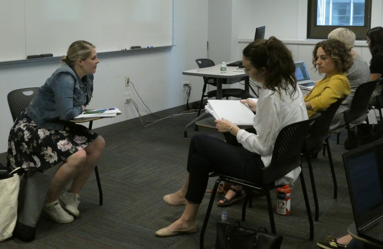 Students in a small circle group, sitting, listening, and speaking