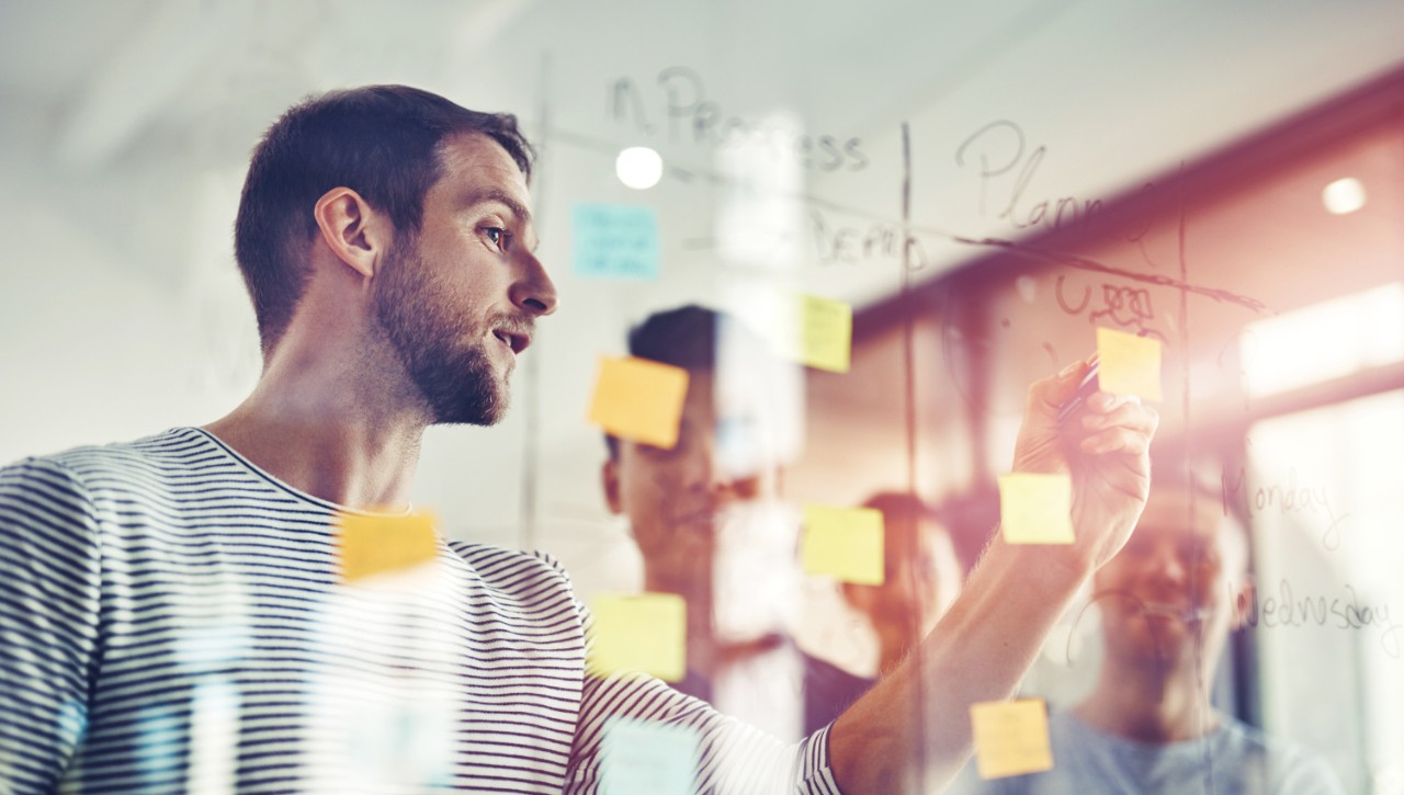 A project management master’s degree student writes on a glass dry erase board.