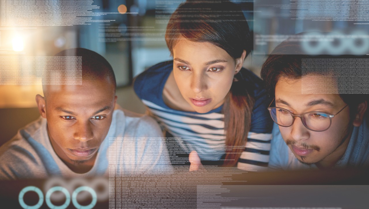 Online management and systems master’s degree students huddle around a computer screen while engaging in online learning.