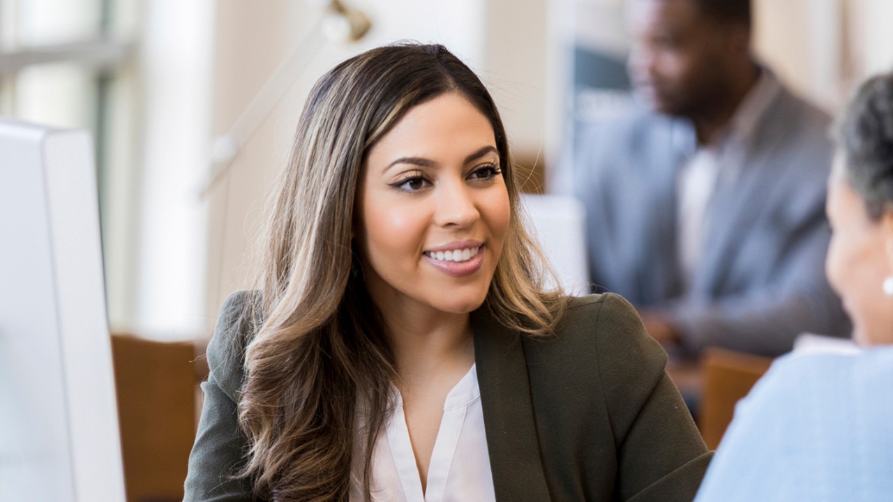 A financial planner sits at her desk while meeting with a client.