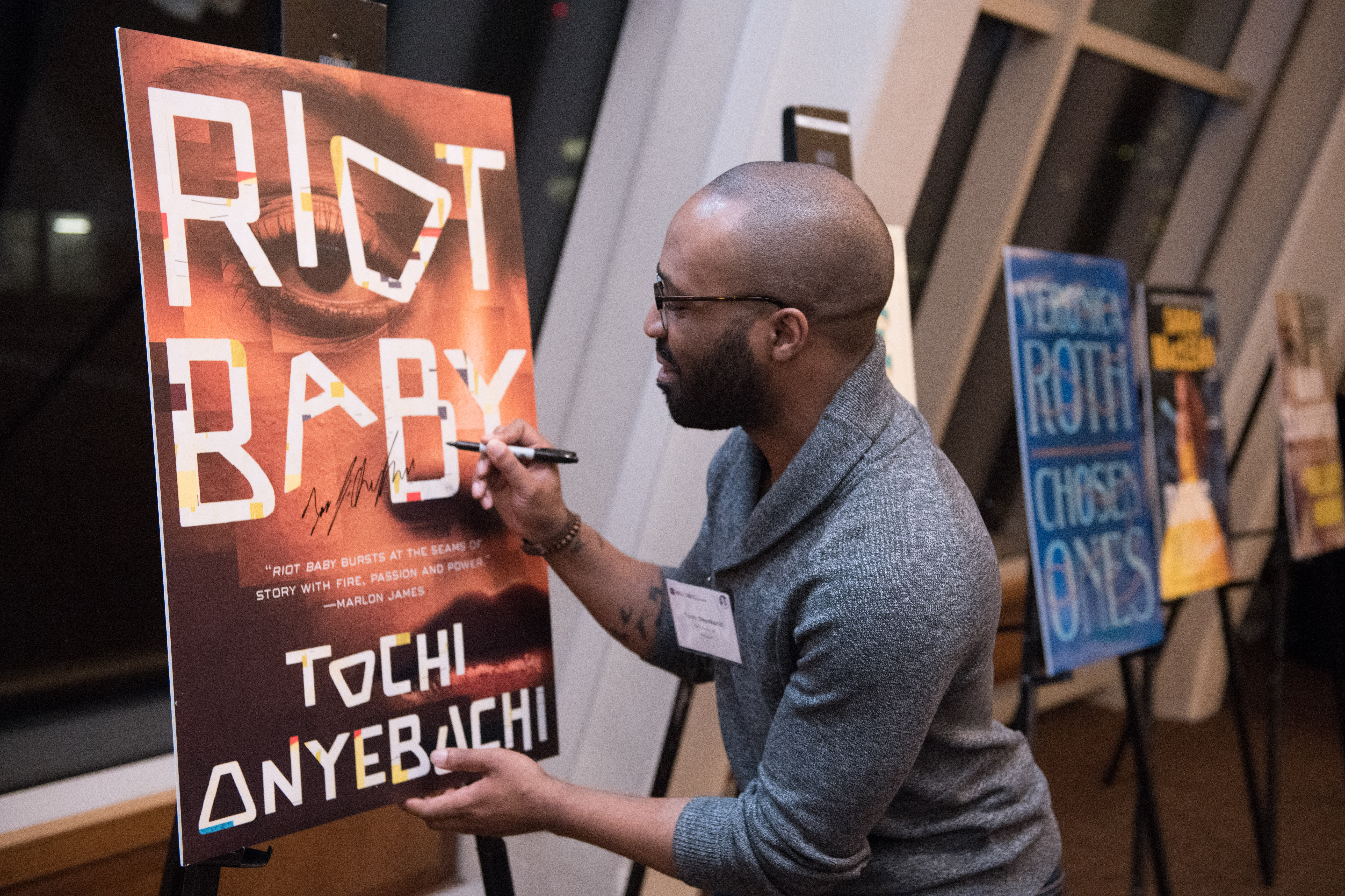 Author Tochi Onyebuchi signs a poster of his book cover (Riot Baby)