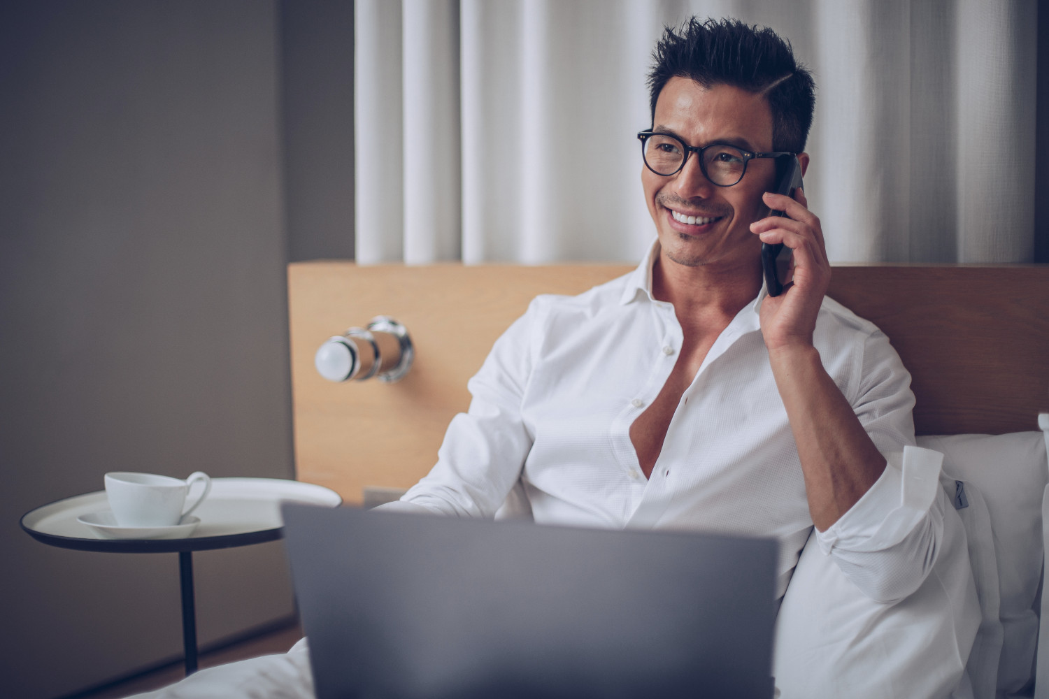 Man on phone and laptop in hotel bed