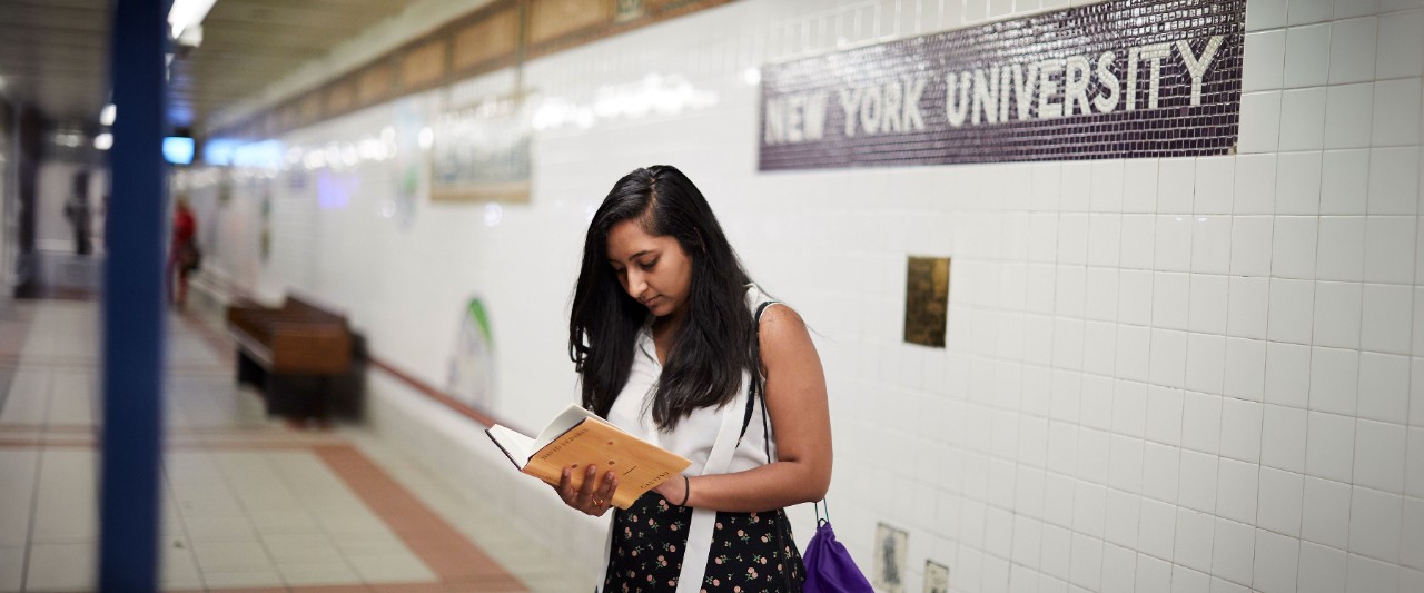 Student waiting at New York University Subway stop reading a book.